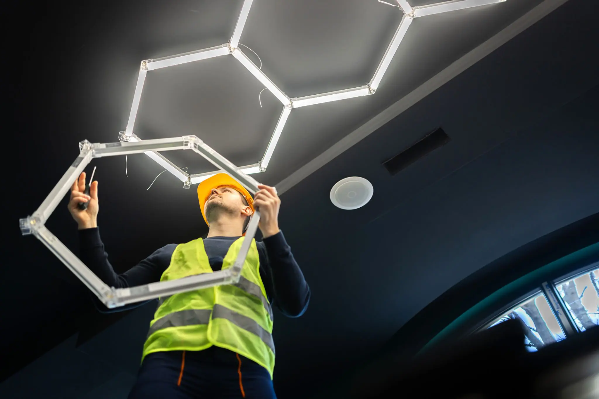 Worker installing hexagonal ceiling light fixture.