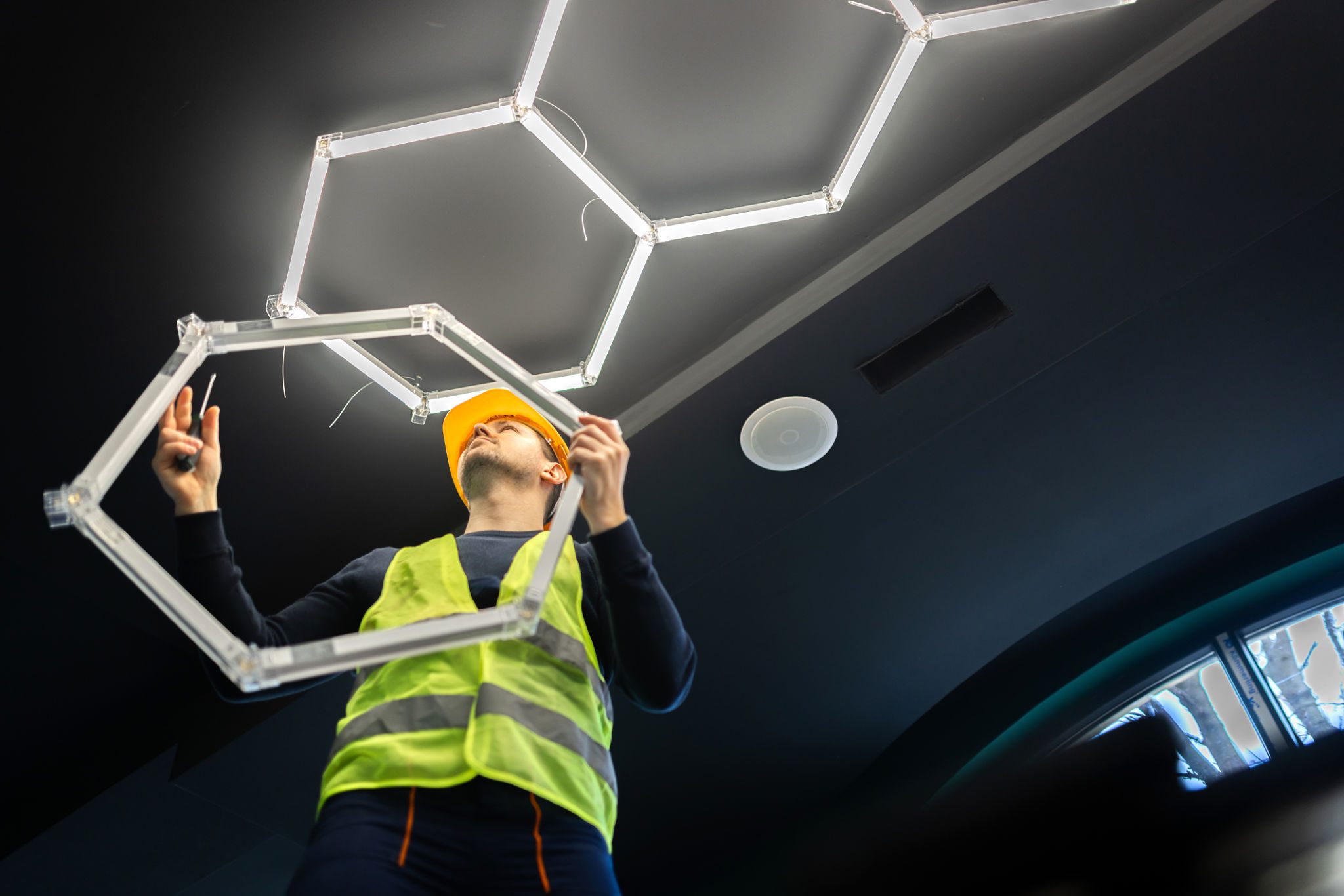 Worker installing hexagonal ceiling light fixture.